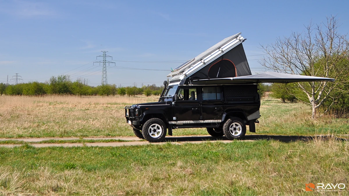 Klasyczny Land Rover Defender 110 z podniesionym dachem Alu-Cab Icarus i rozłożoną markizą, realizacja RAYO